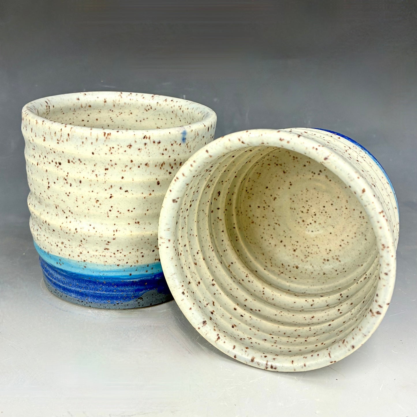 Speckled ceramic container with blue accent on a gray background