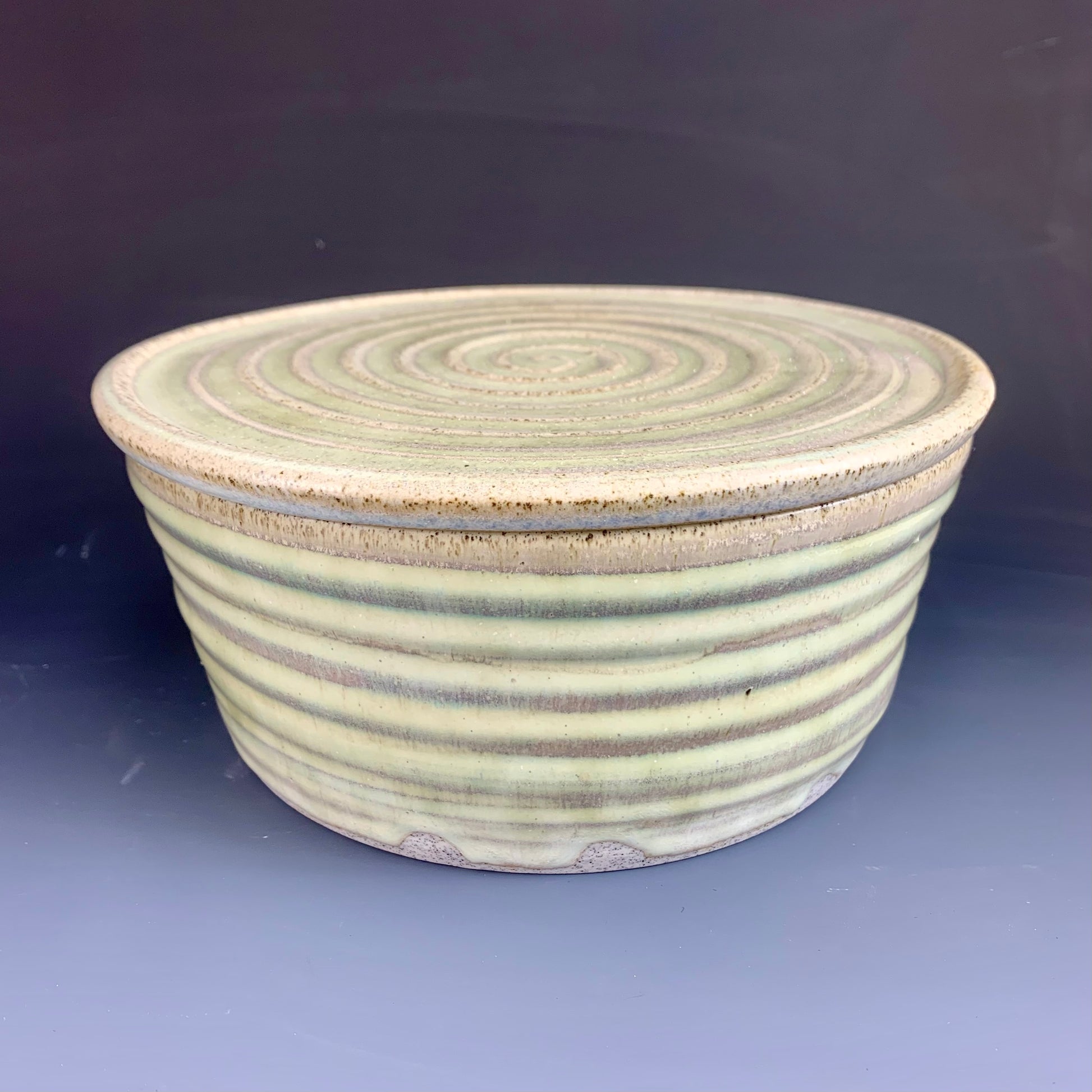 Green and Gray ceramic storage container on dark background, lid on