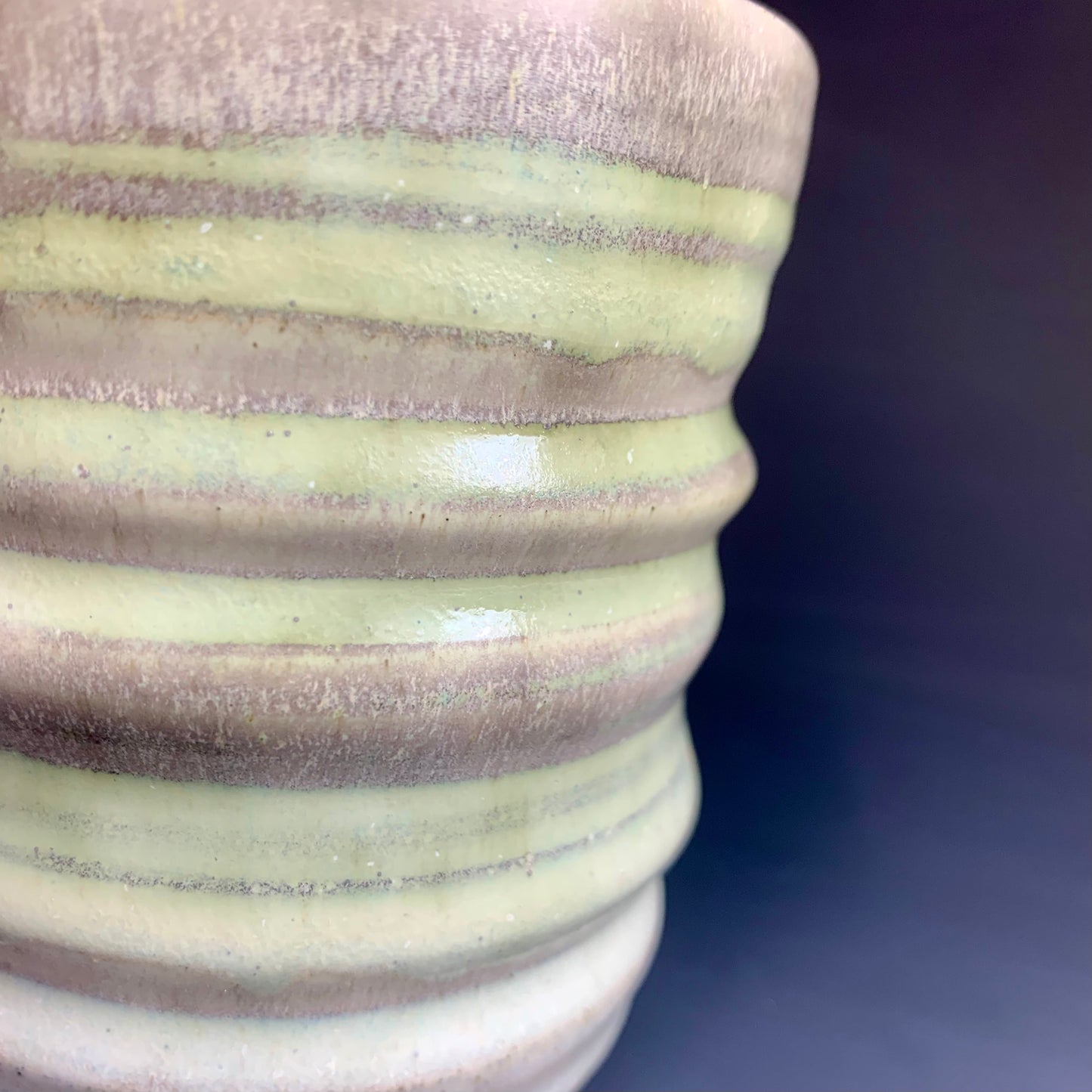 Detail of glaze color variation of Green and Gray Wheel thrown cup on dark background