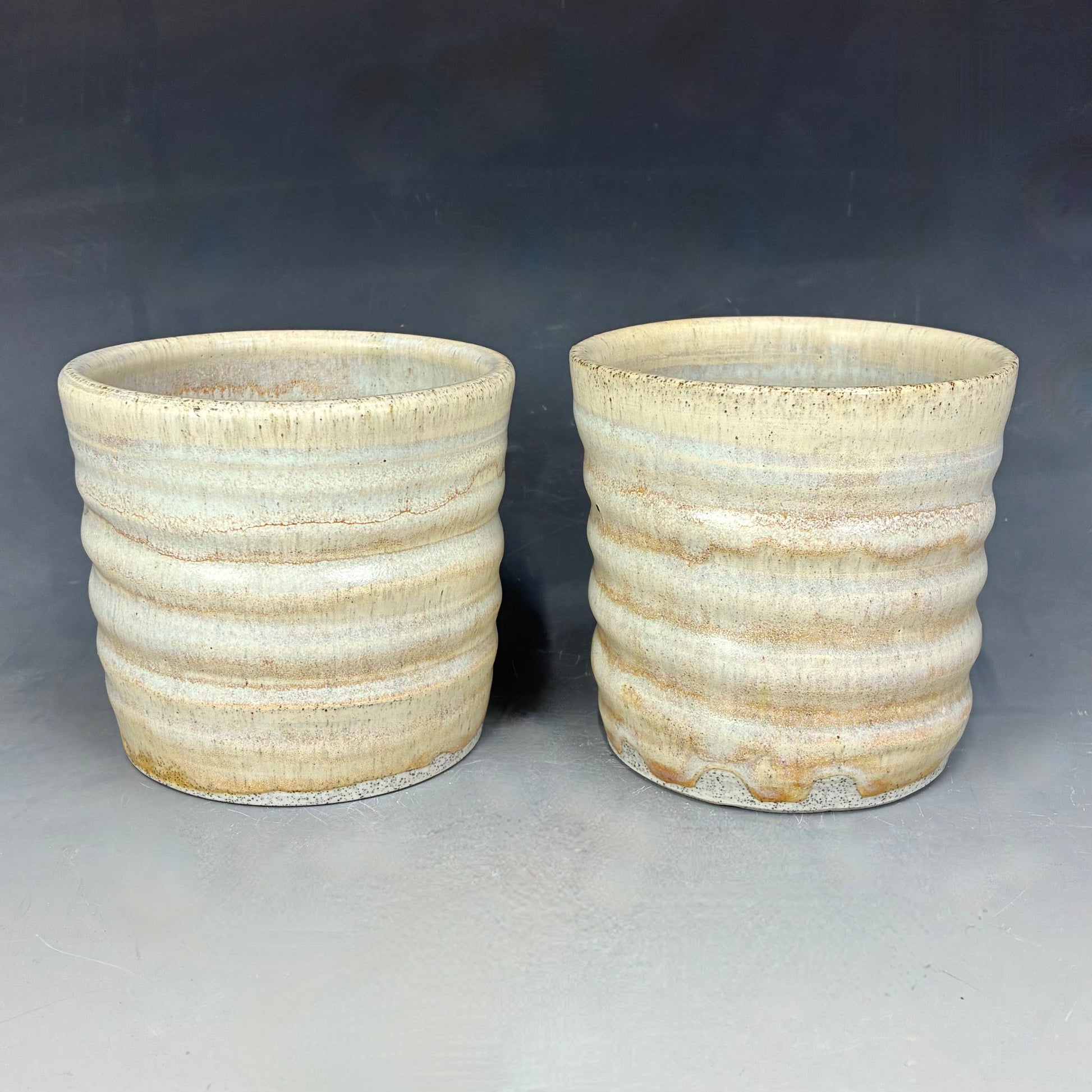 Two ceramic pots with ribbed texture on a gray background