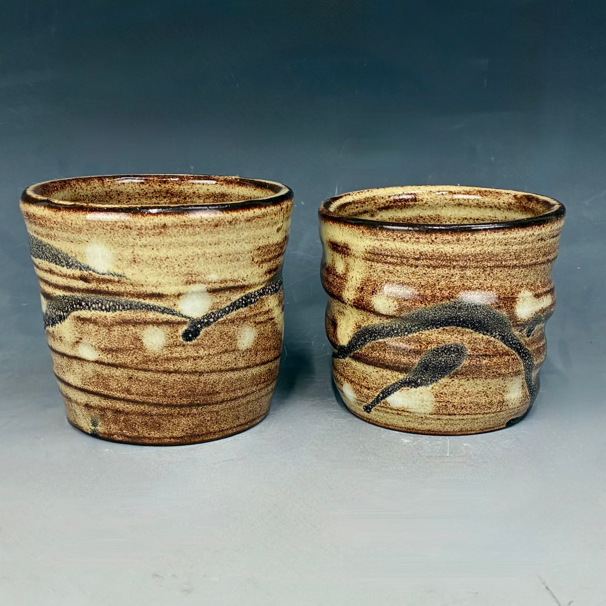 Two ceramic cups with brown and beige glaze on a gray background