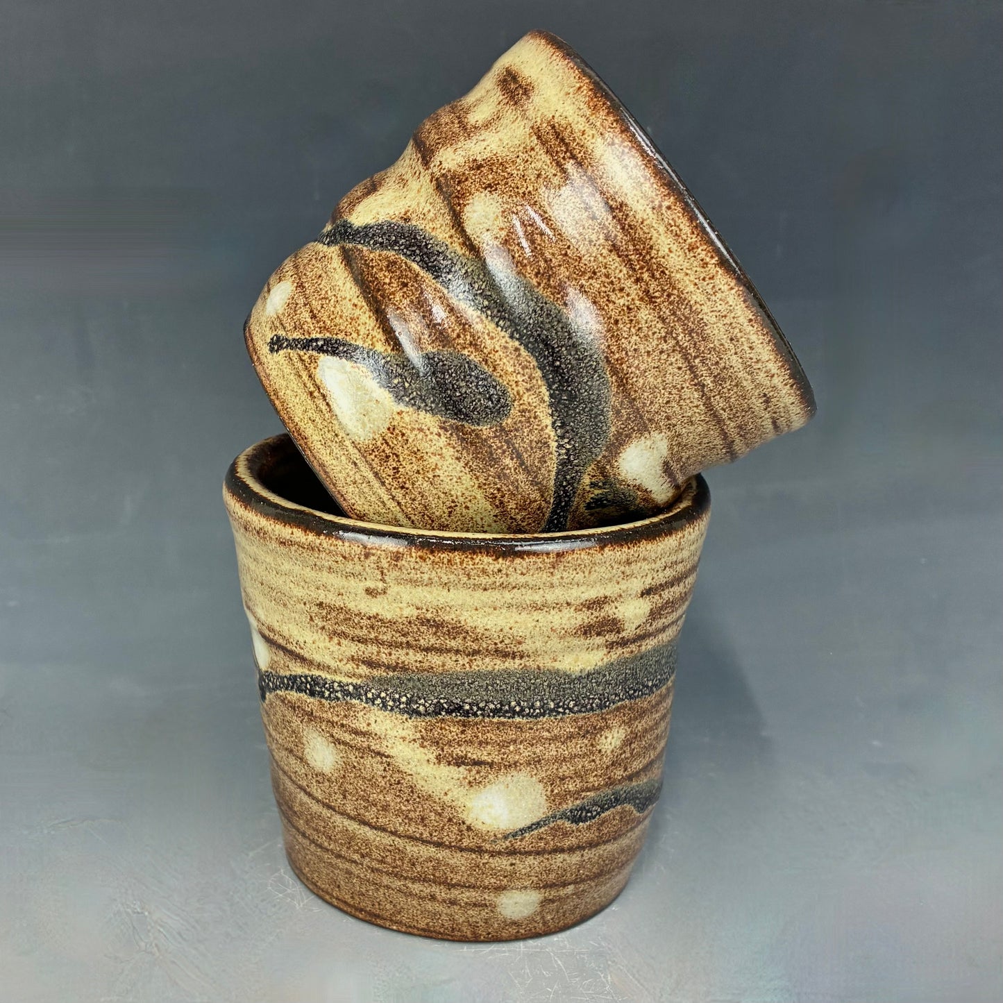 Two ceramic cups with a marbled brown and beige design on a gray background