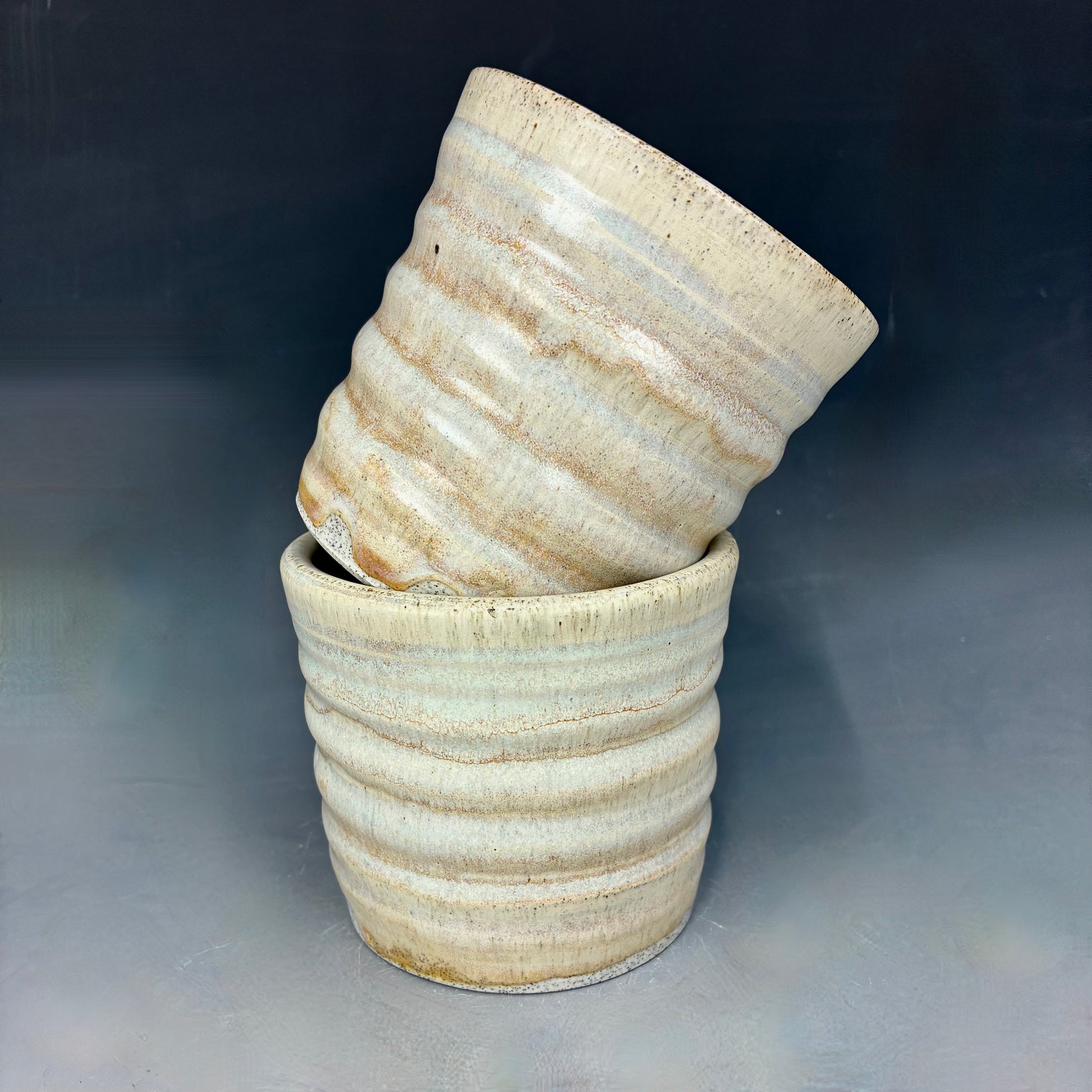 Two light yellow ceramic cups with textured surface on a gray background