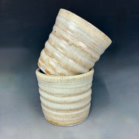 Two light yellow ceramic cups with textured surface on a gray background