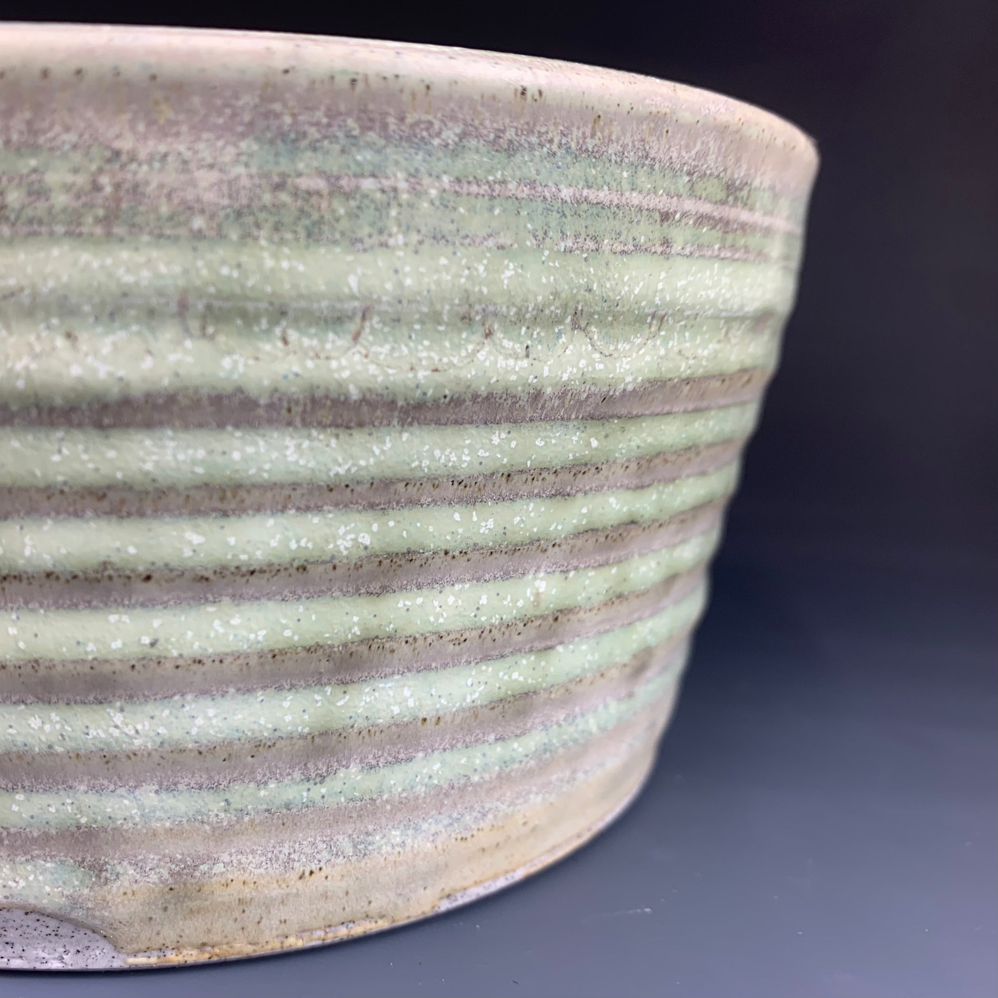 Detail of glaze color variation of Green and Gray wheel thrown bowl on dark background