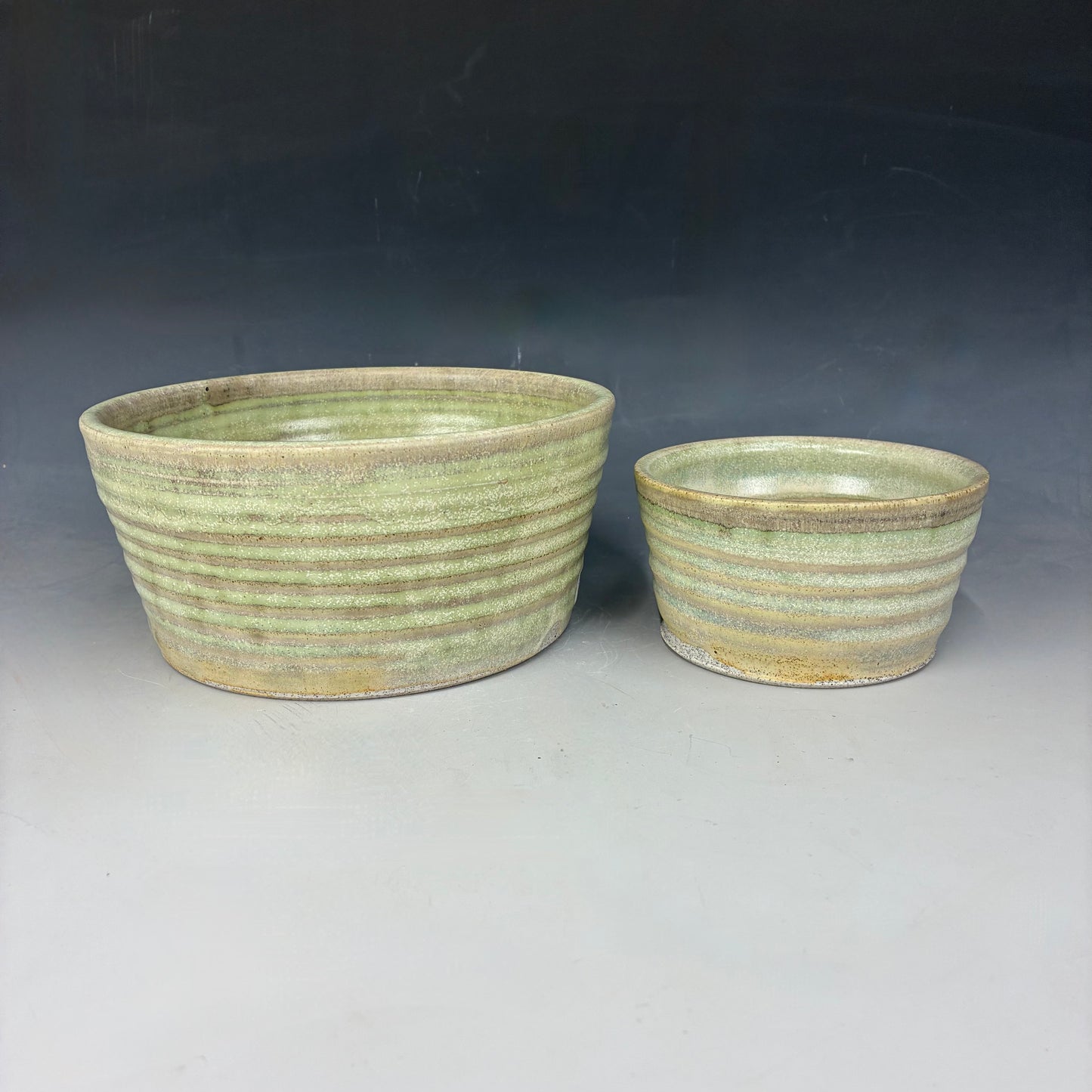 Two ceramic pots with greenish-brown glaze on a gray background