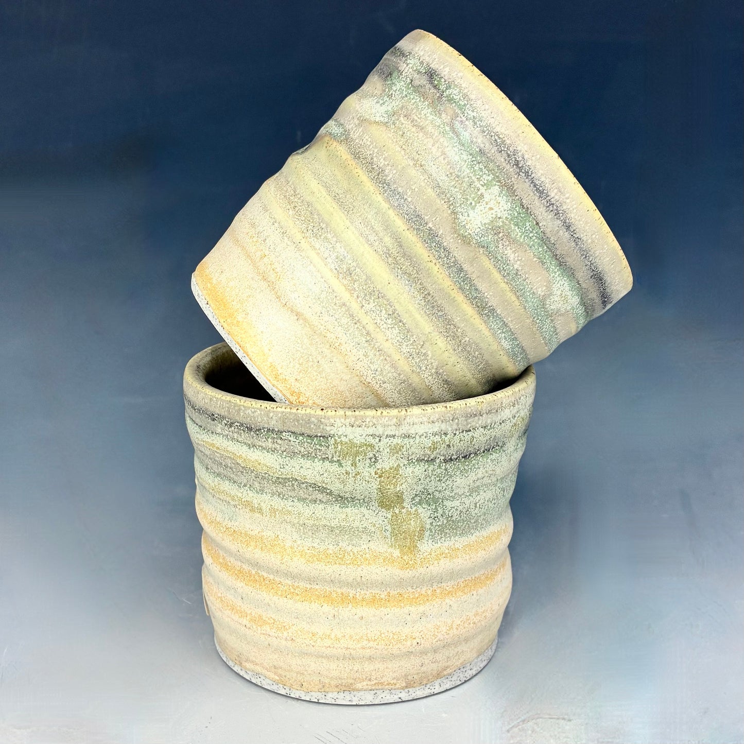 Two ceramic pots with striped patterns on a gradient blue and gray background