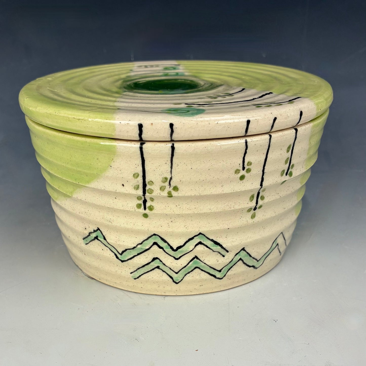 Ceramic container with green and black patterns on a gray background