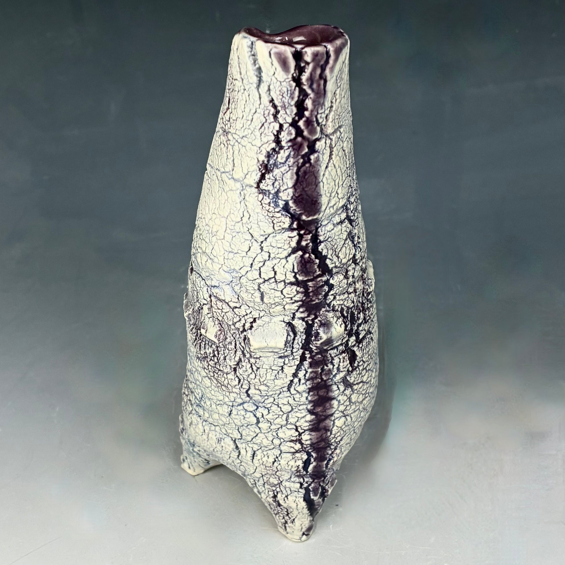 Ceramic vase with textured surface and purple accents on a gray background