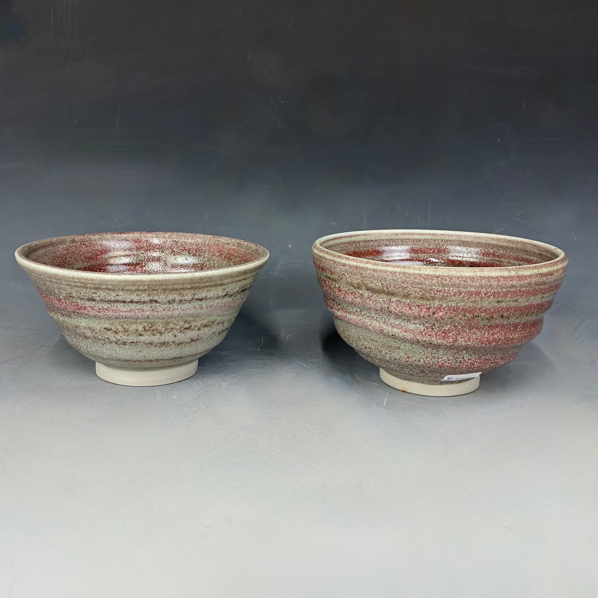 Two ceramic bowls with a speckled glaze on a gray background