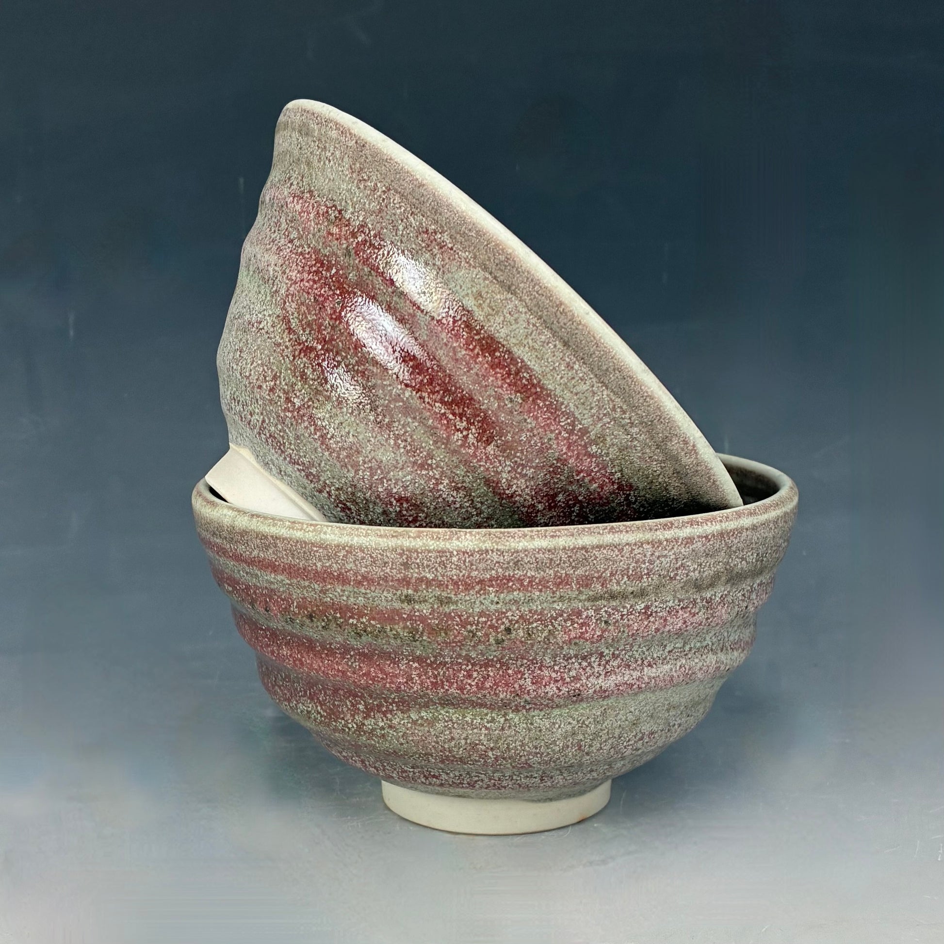 Two ceramic bowls with a speckled glaze on a gradient background