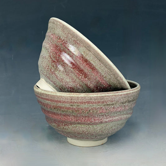 Two ceramic bowls with a speckled glaze on a gradient background