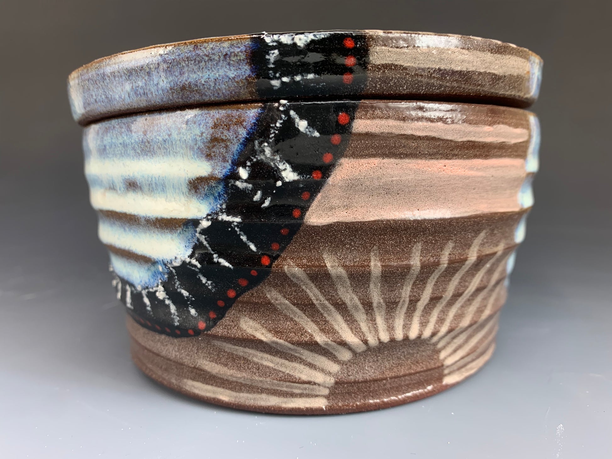 Side view of Brown, White, Black and Red decorated ceramic storage container, Lid on, sun decoration visible