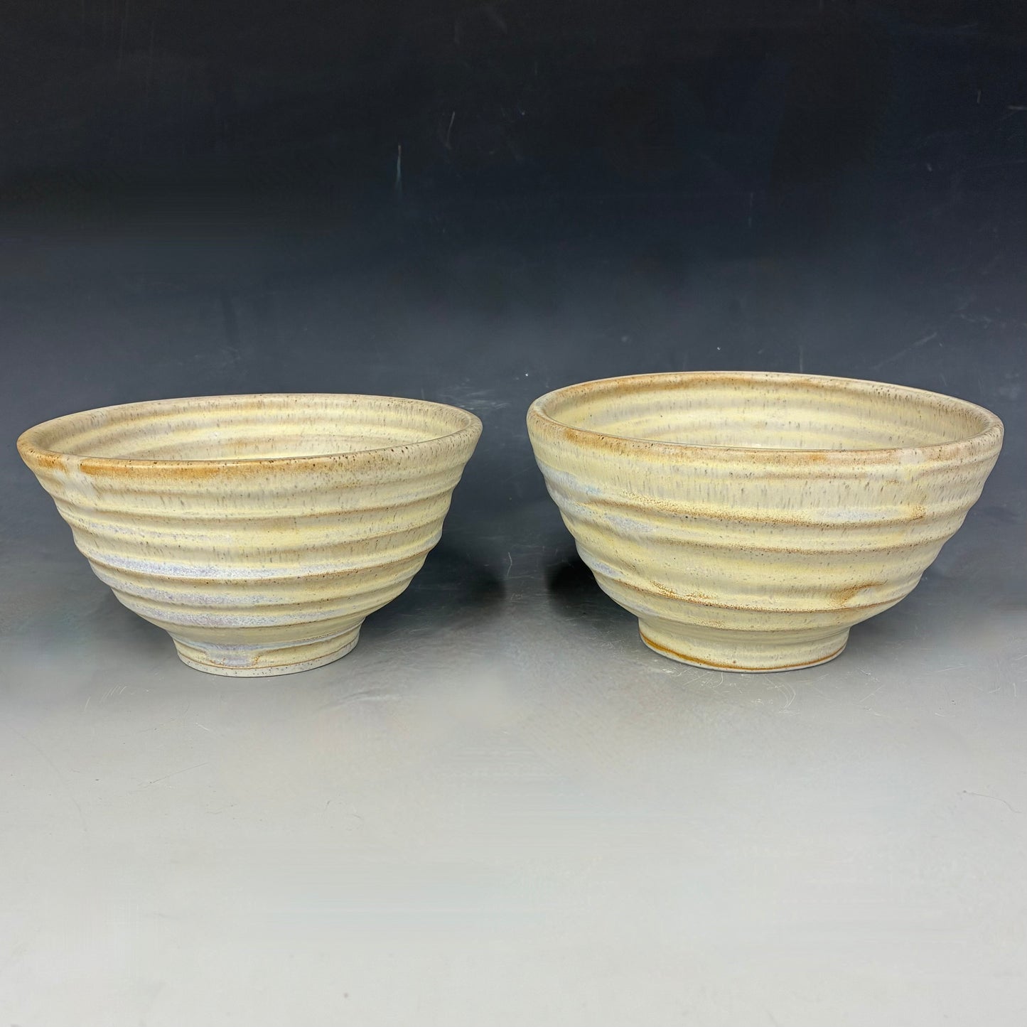 Two ceramic bowls with ribbed texture on a dark background