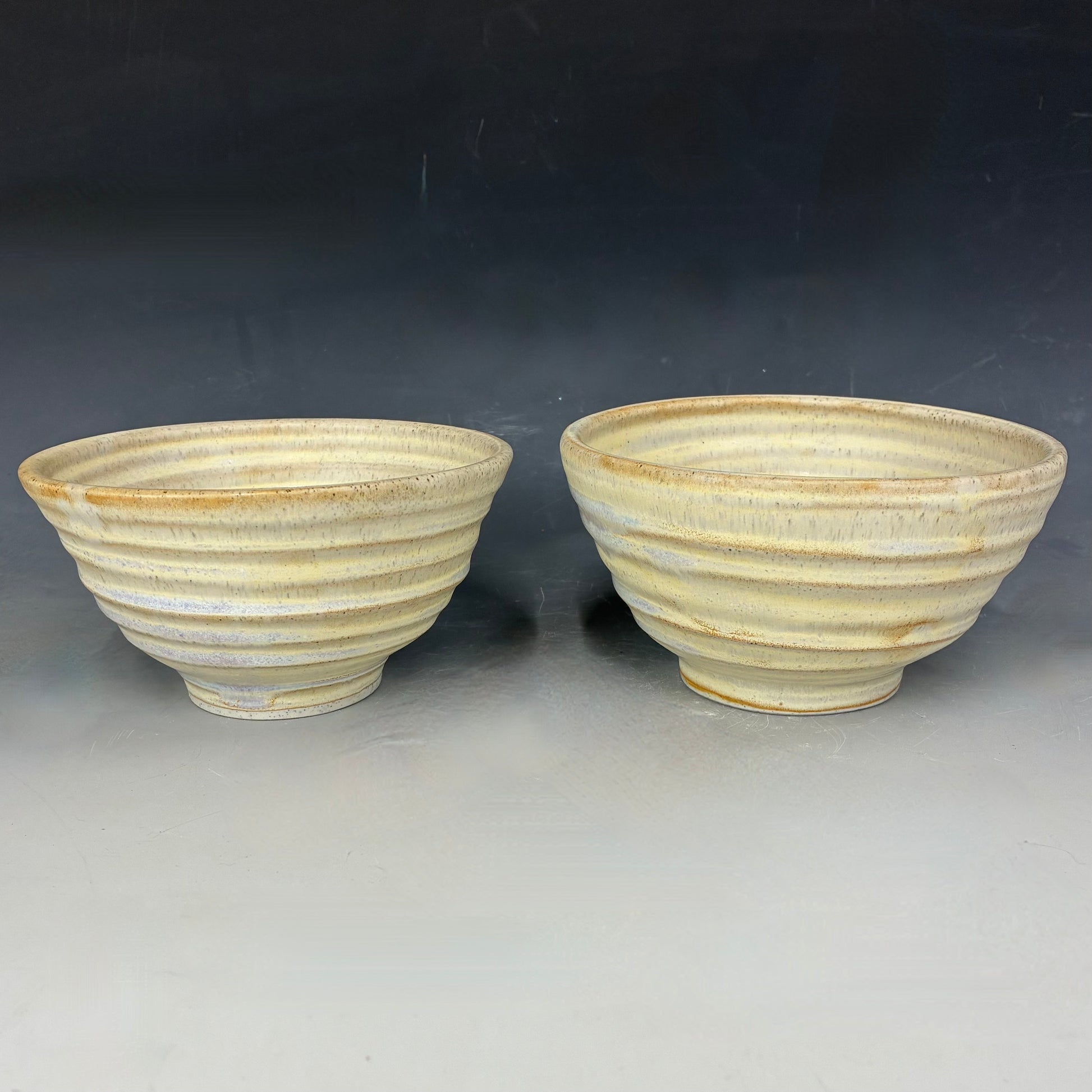 Two ceramic bowls with ribbed texture on a dark background